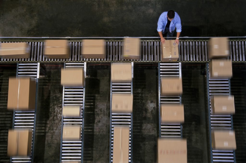 Warehouse employees organizing cardboard boxes moving on a conveyor belt in a distribution